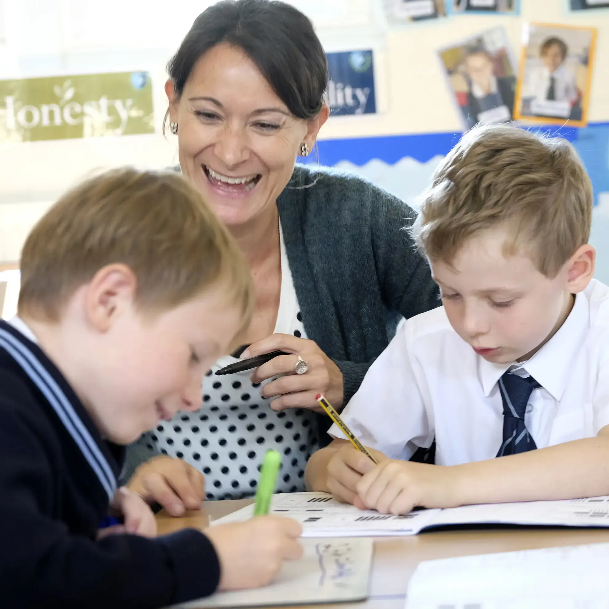 Teacher sitting with two students, one working in a book and the other on a whiteboard