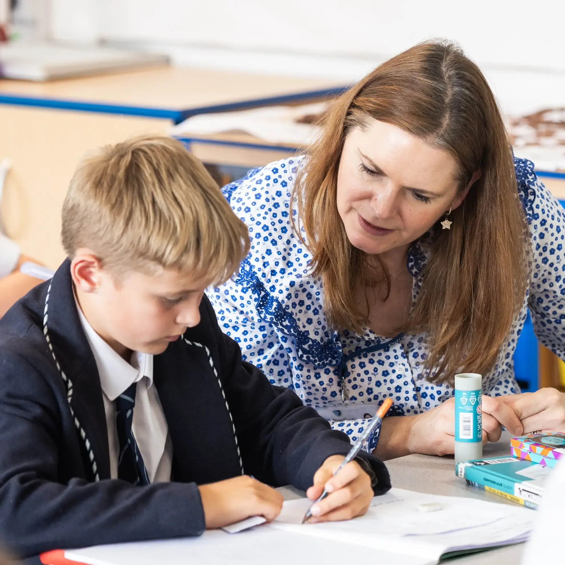 Teacher speaking to student as they write in an exercise book