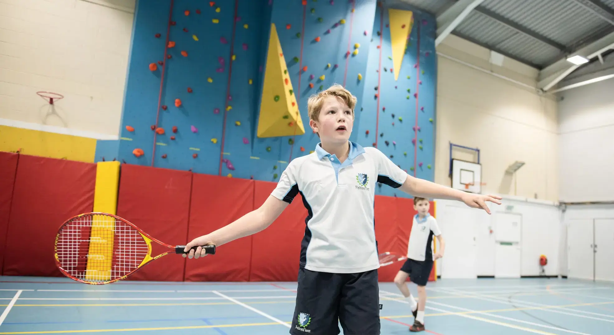 Student holding tennis racquet in front of climbing wall
