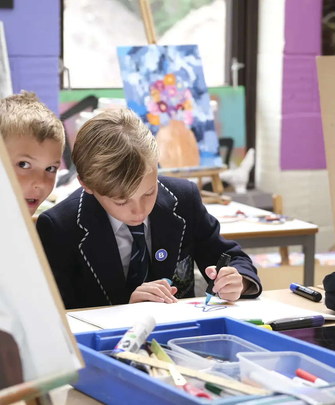 One student drawing while another peeks out from behind a canvas