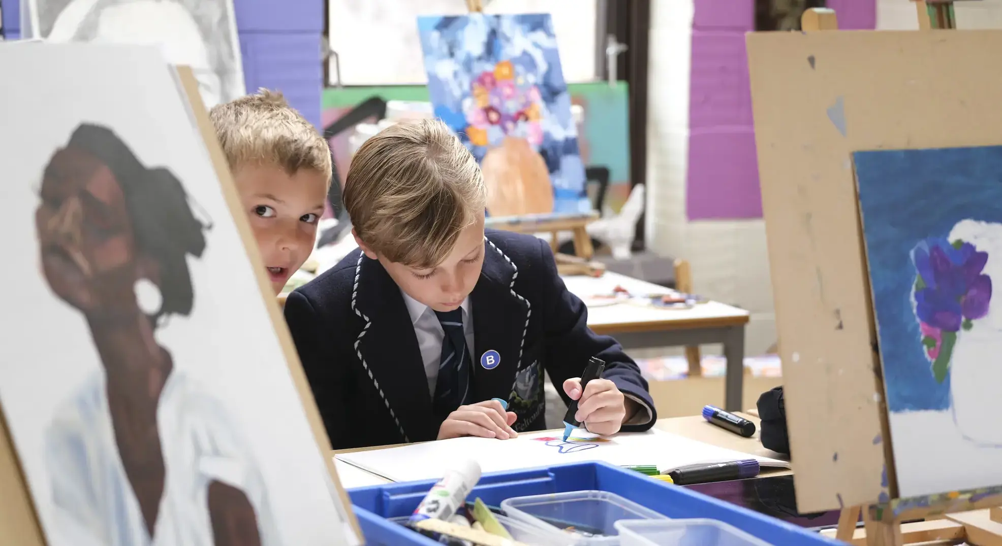 One student drawing while another peeks out from behind a canvas