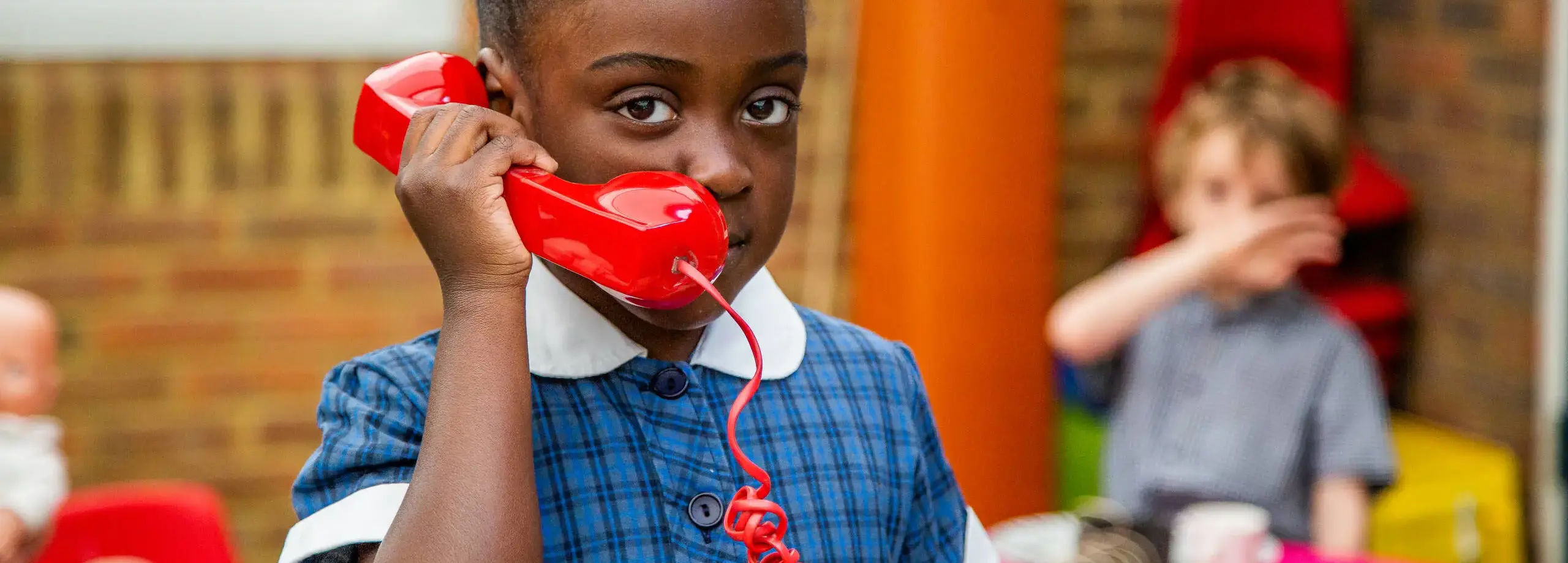 Pre-prep pupil roleplaying phone call with large red handset