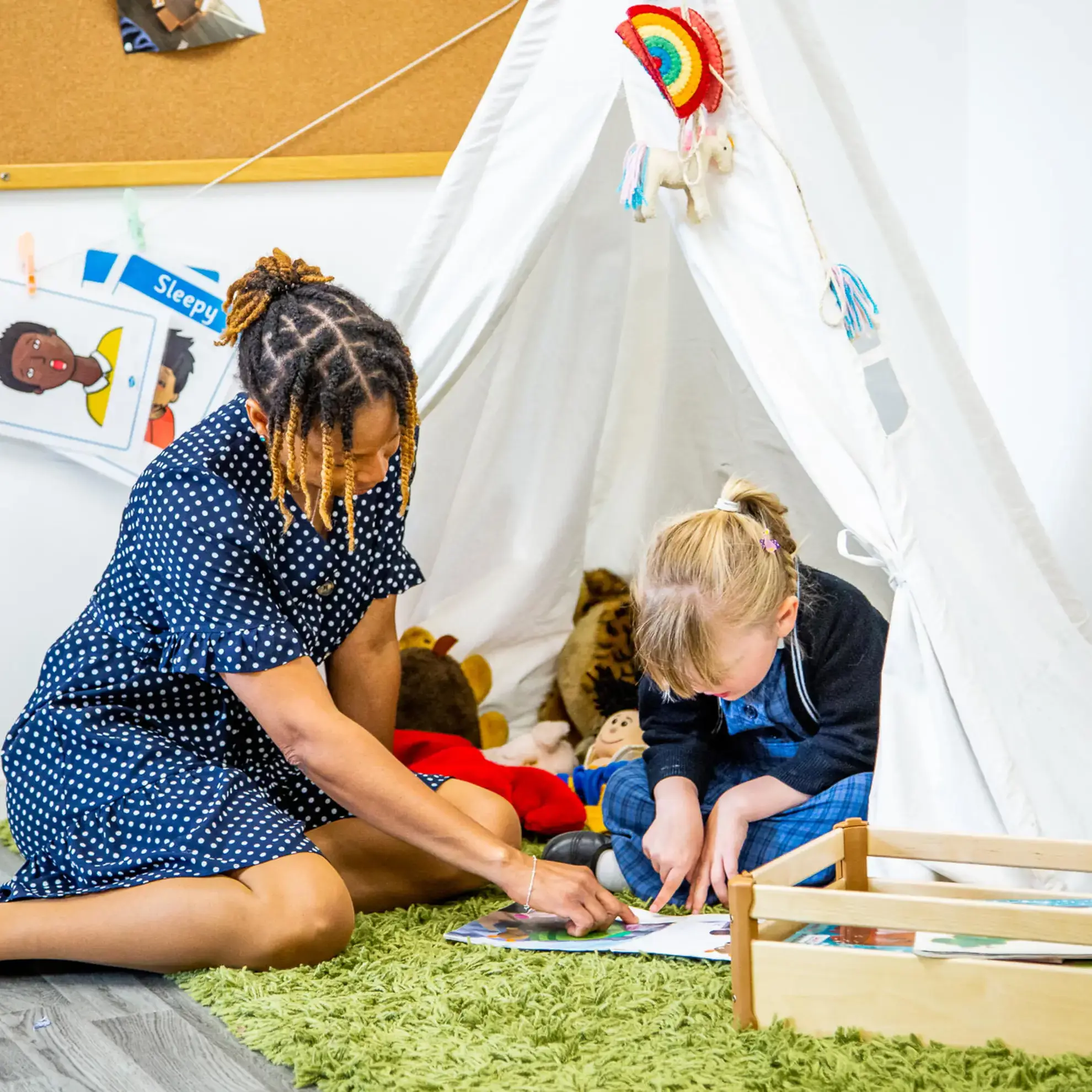 Pupil and teacher reading a book under a tipi