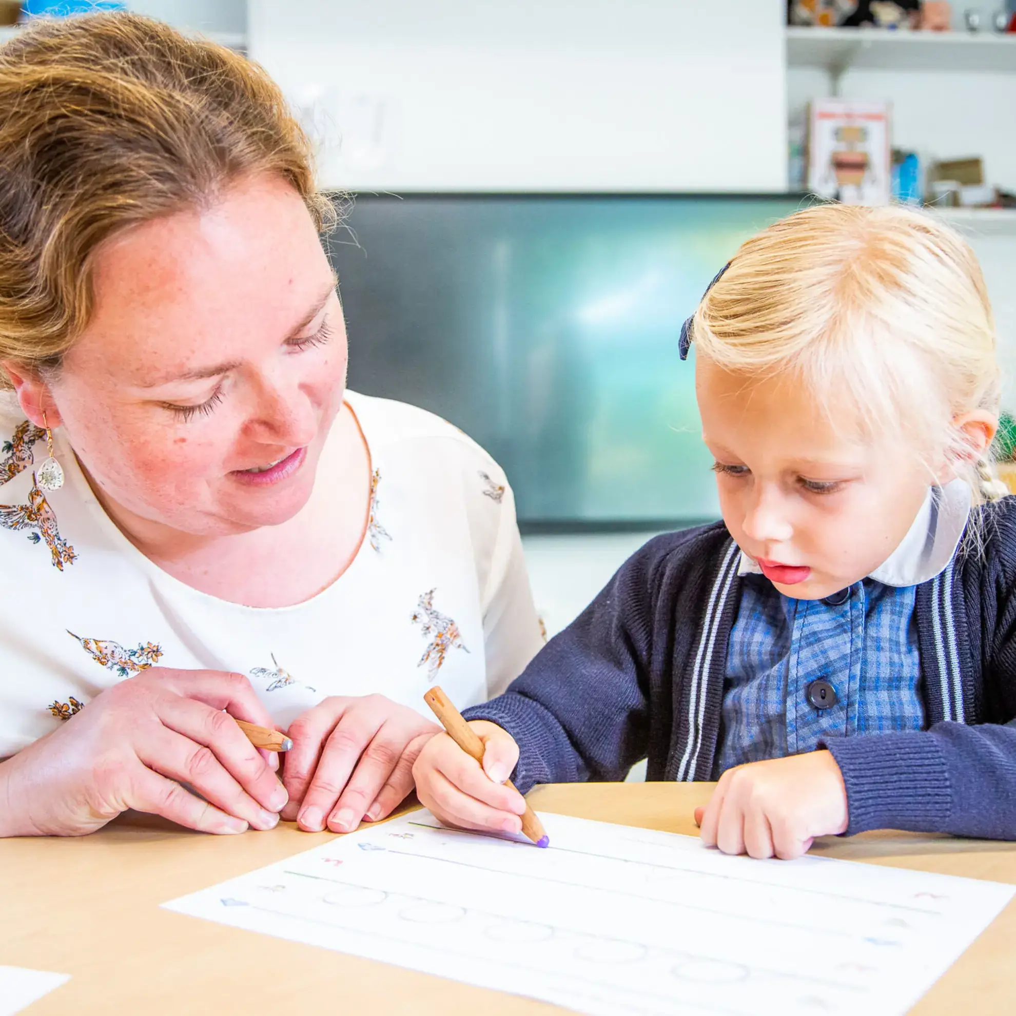 Teacher supervising student while they write with a purple crayon