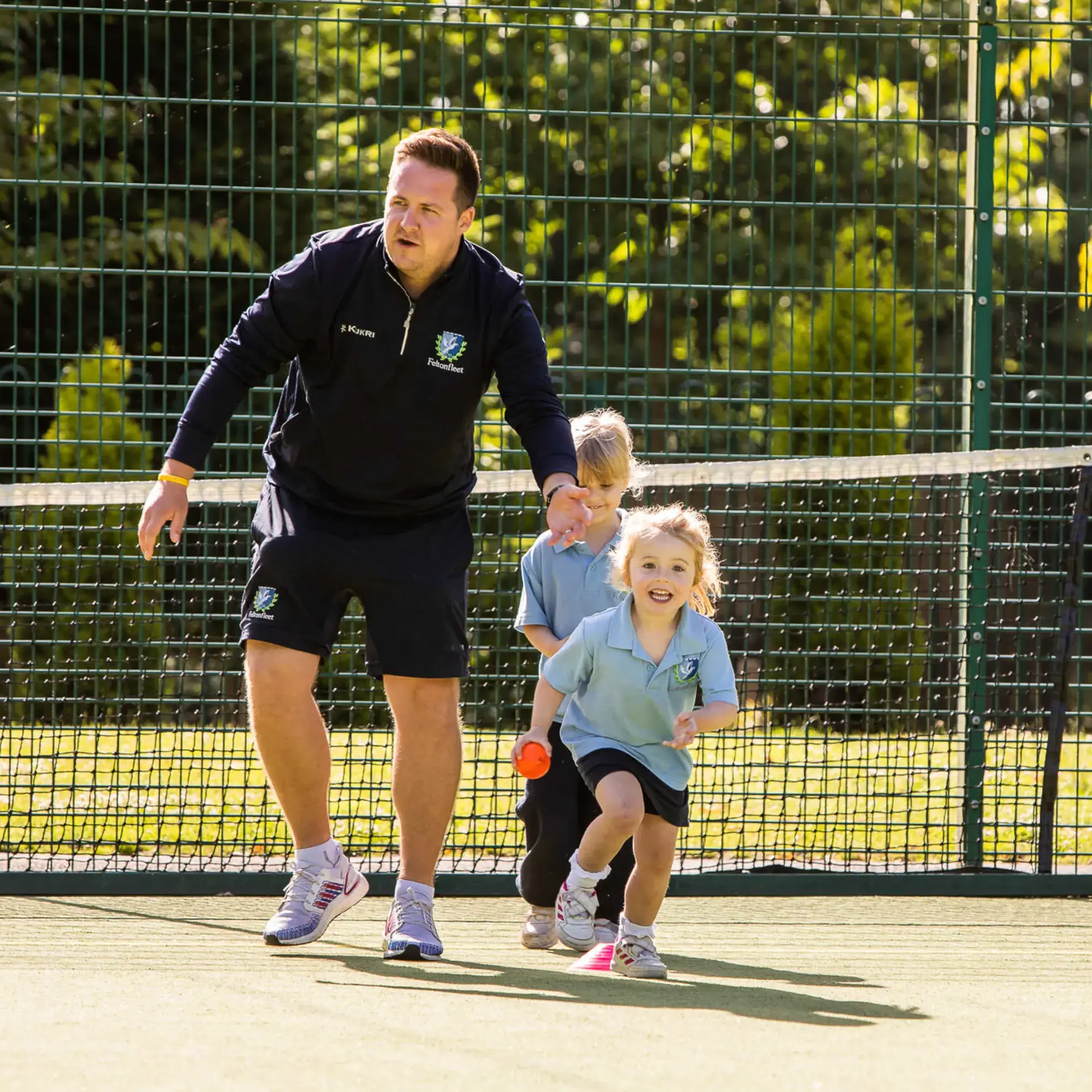 Student running, holding an orange ball, encouraged by a teacher