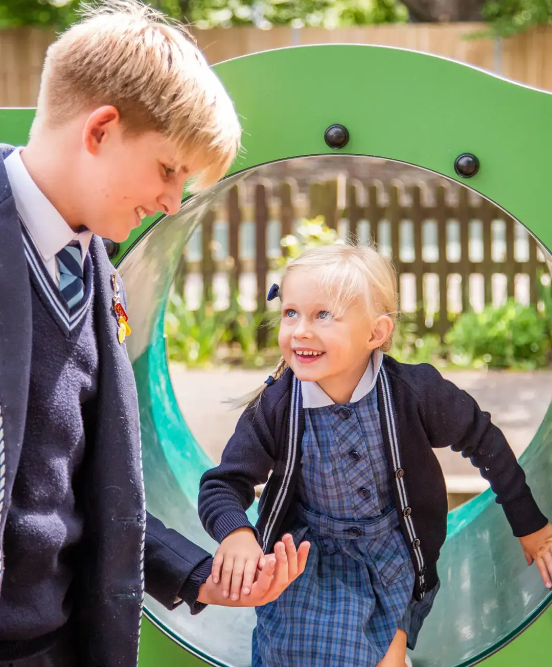 Student helping younger peer out of some playground apparatus 