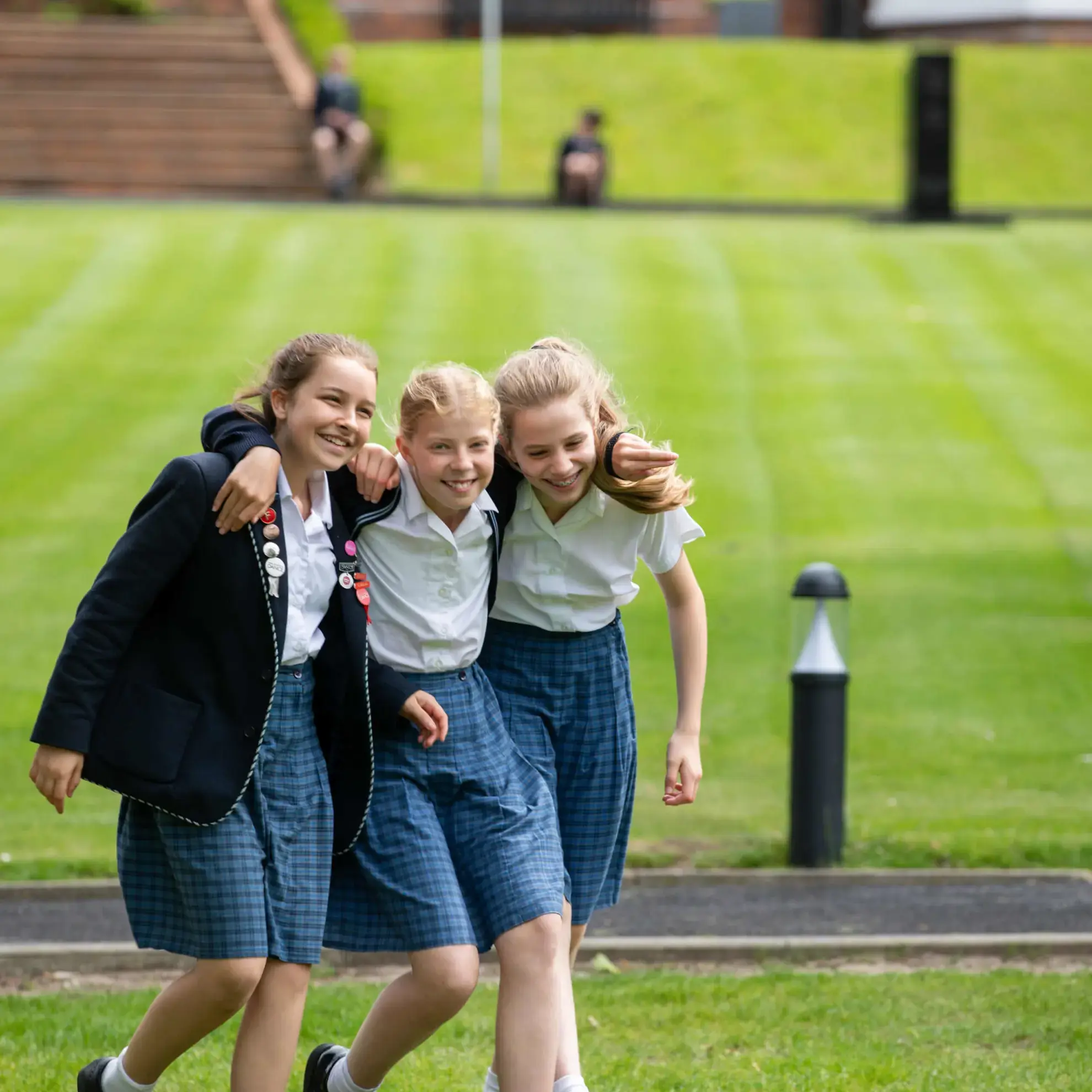 Three students walking arm-in-arm over a field